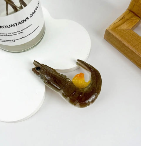 Shrimp-shaped soap with a yellow yolk on a white surface next to a cylindrical container.