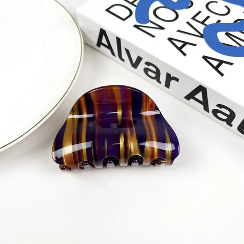 A glossy claw hair clip with vertical marbled stripes of purple, amber, and brown